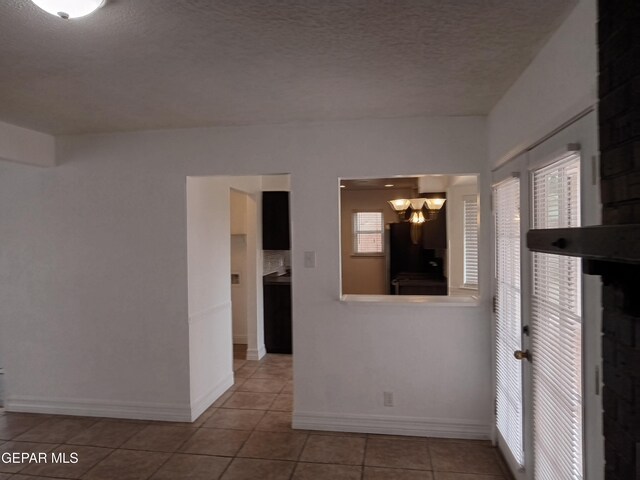 tiled empty room featuring baseboards, a chandelier, and a textured ceiling