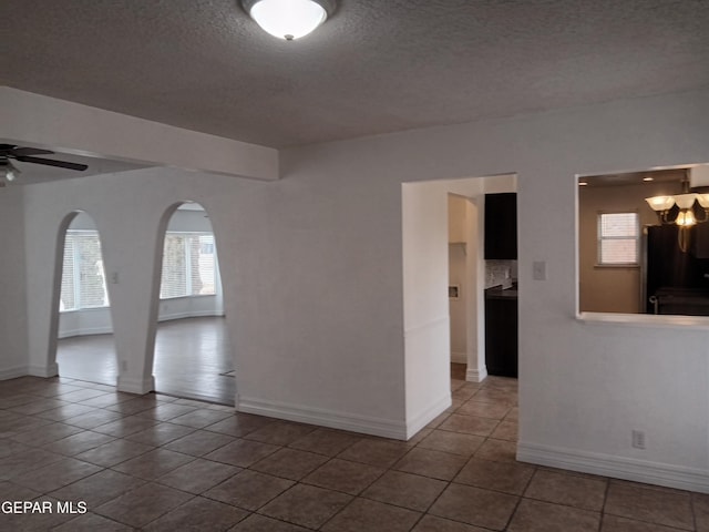 unfurnished room with arched walkways, a textured ceiling, tile patterned floors, and a ceiling fan