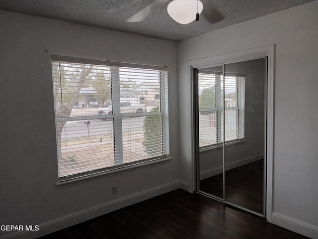 interior space featuring a closet, a textured ceiling, baseboards, ceiling fan, and dark wood-style flooring