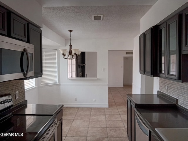 kitchen featuring appliances with stainless steel finishes, dark countertops, light tile patterned floors, visible vents, and an inviting chandelier