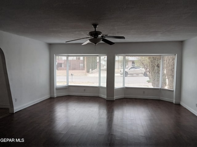 empty room with a ceiling fan, a textured ceiling, baseboards, arched walkways, and dark wood-style flooring
