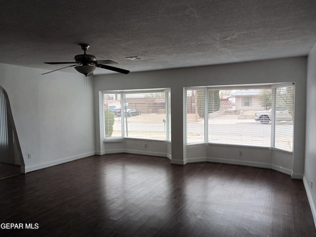 spare room featuring a textured ceiling, visible vents, baseboards, ceiling fan, and dark wood finished floors