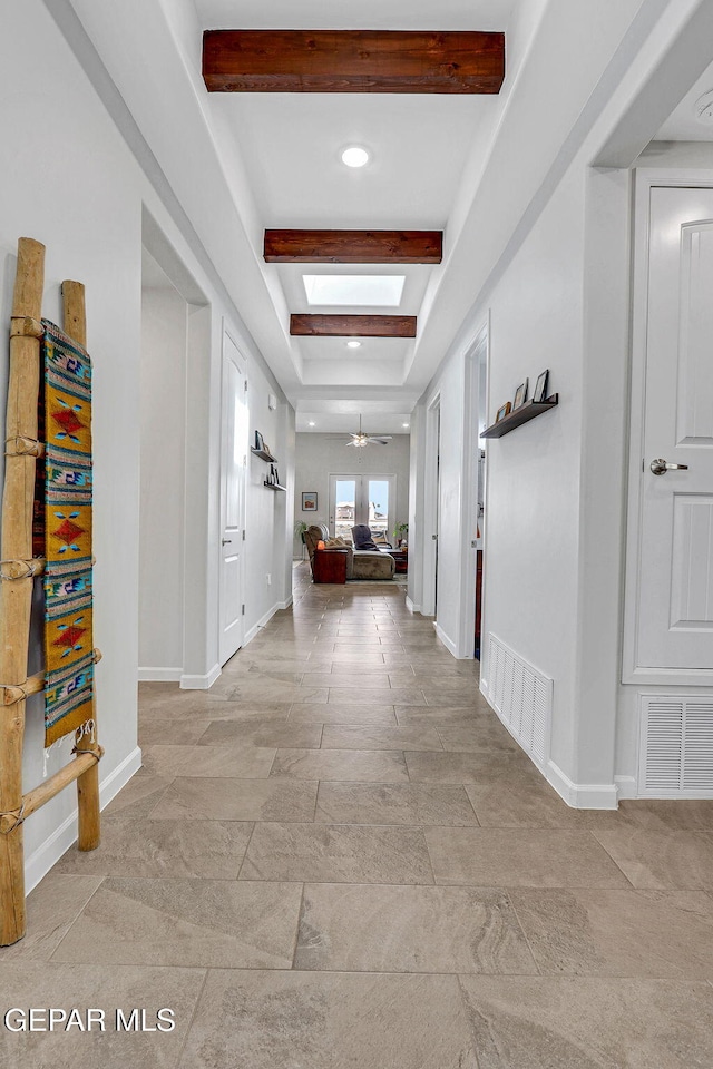 hall featuring baseboards, visible vents, stone finish flooring, and beam ceiling