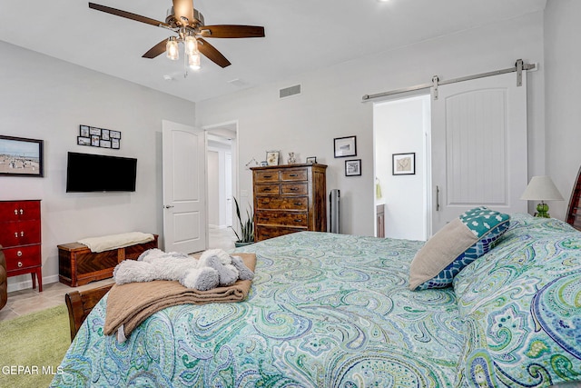 bedroom with a barn door, connected bathroom, light tile patterned floors, ceiling fan, and visible vents