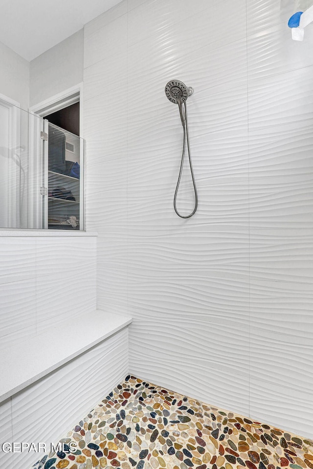 full bathroom featuring a tile shower and stone finish flooring