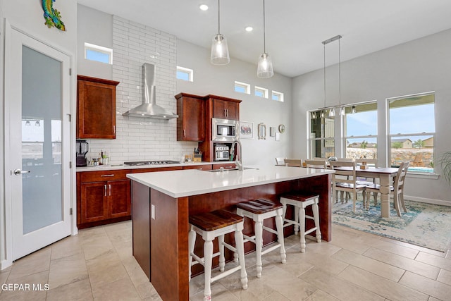 kitchen with wall chimney range hood, a sink, decorative backsplash, light countertops, and appliances with stainless steel finishes