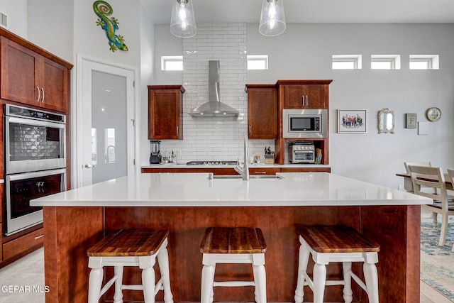 kitchen featuring wall chimney range hood, tasteful backsplash, stainless steel appliances, light countertops, and a kitchen bar