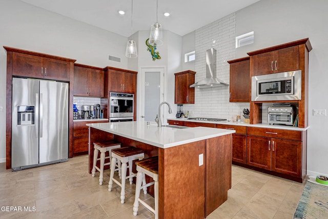 kitchen with a sink, backsplash, wall chimney exhaust hood, appliances with stainless steel finishes, and visible vents