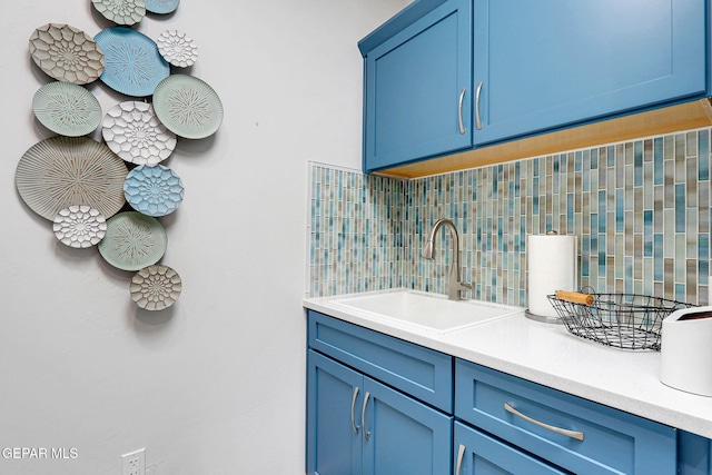 kitchen with blue cabinetry, decorative backsplash, a sink, and light countertops