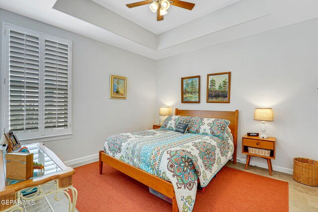 bedroom with a raised ceiling, a ceiling fan, baseboards, and tile patterned floors