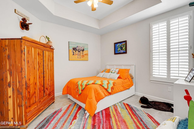 bedroom featuring a ceiling fan, baseboards, tile patterned flooring, and a raised ceiling
