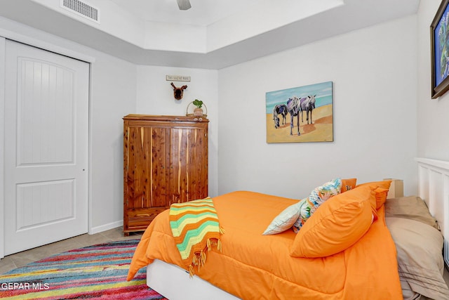 tiled bedroom with a tray ceiling, visible vents, and ceiling fan
