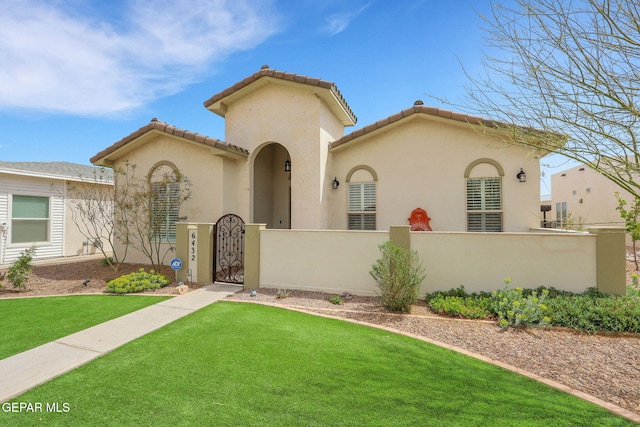 mediterranean / spanish-style house featuring a gate, a fenced front yard, stucco siding, a tile roof, and a front yard