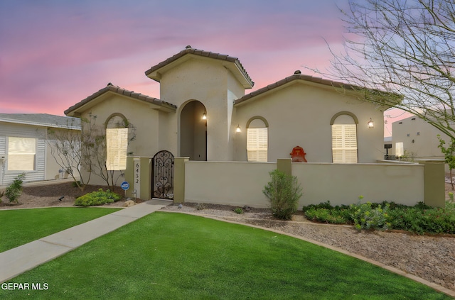 mediterranean / spanish home with a gate, a fenced front yard, a front lawn, a tiled roof, and stucco siding