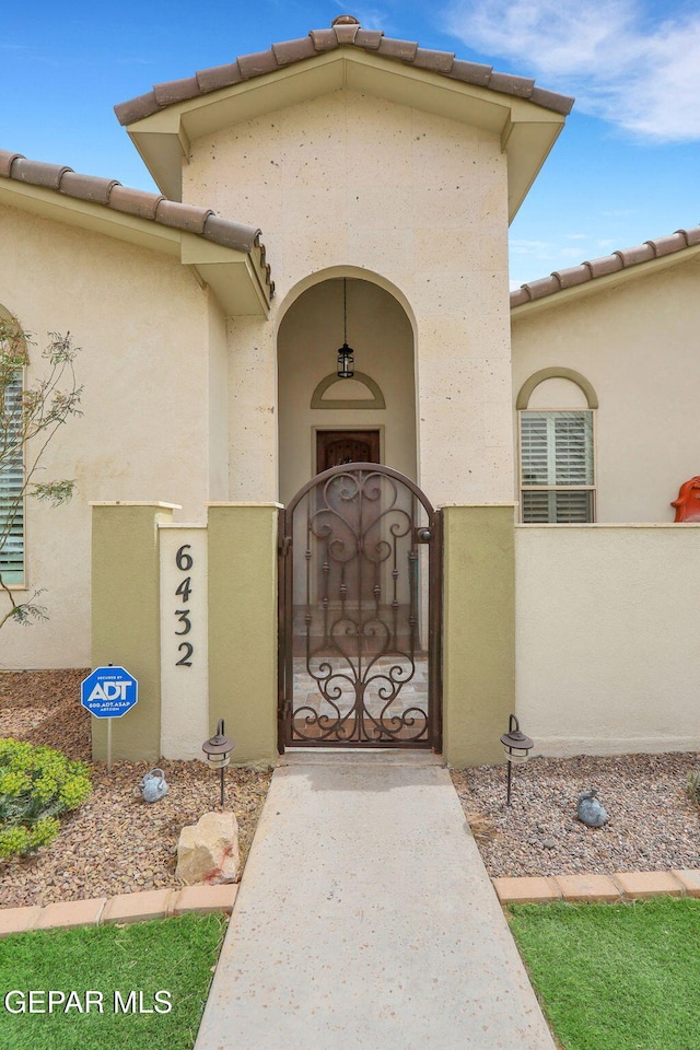 entrance to property with a gate, a tile roof, stucco siding, and fence