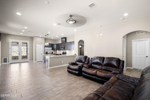 living area with visible vents, ceiling fan, light wood finished floors, and arched walkways