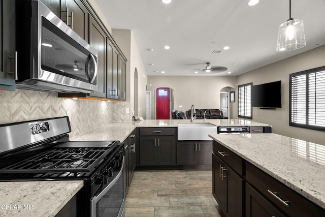 kitchen featuring a peninsula, open floor plan, stainless steel appliances, arched walkways, and a sink