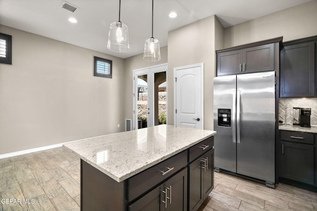 kitchen with light stone countertops, light wood-style flooring, visible vents, stainless steel fridge, and decorative backsplash