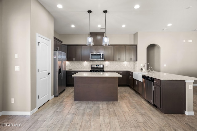 kitchen featuring arched walkways, a sink, light wood-style floors, a peninsula, and stainless steel appliances