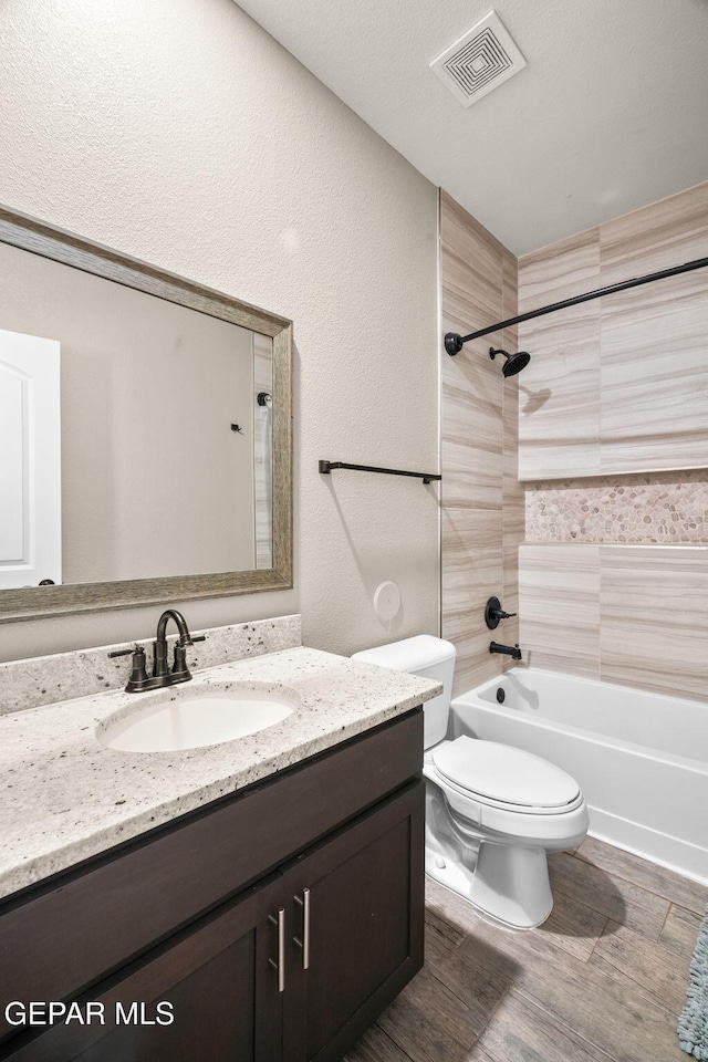 bathroom featuring visible vents, toilet, vanity, wood finished floors, and shower / bathtub combination