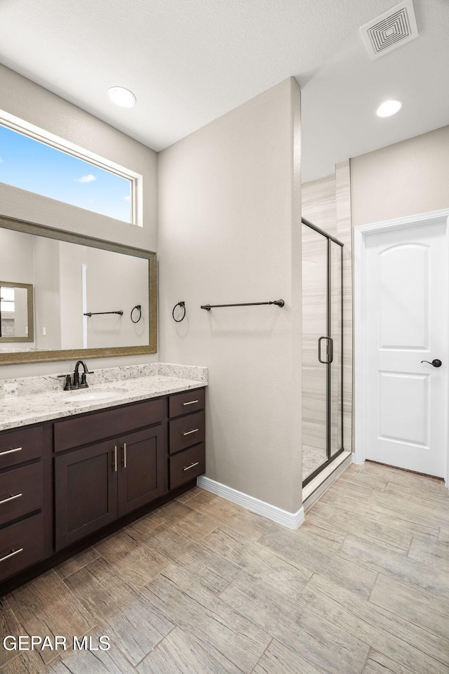 bathroom with visible vents, baseboards, vanity, wood finished floors, and a stall shower
