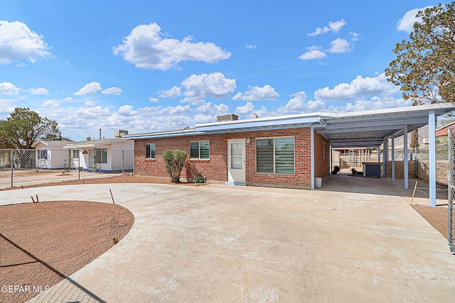 rear view of house featuring a carport, fence, brick siding, and concrete driveway