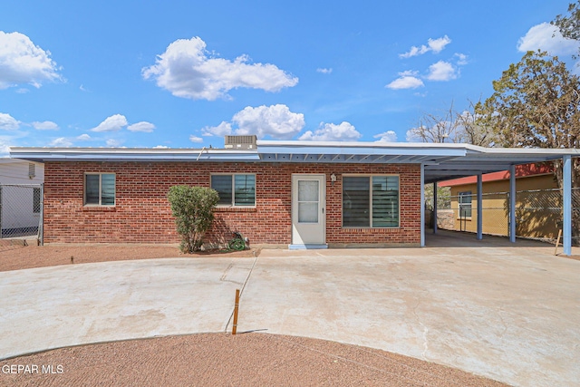 back of property with brick siding, concrete driveway, a carport, and fence
