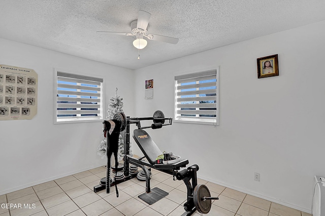 exercise room with a ceiling fan, light tile patterned floors, baseboards, and a textured ceiling