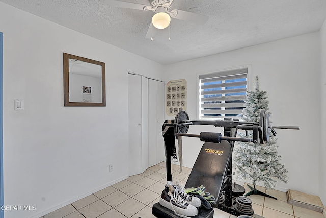 exercise area featuring a ceiling fan, light tile patterned floors, and a textured ceiling