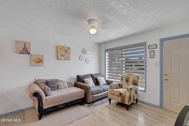 living area with baseboards, a textured ceiling, light wood-style floors, and ceiling fan