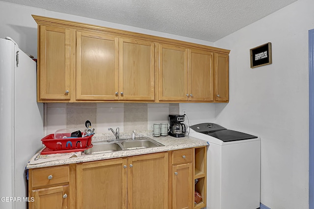 washroom with a textured ceiling, cabinet space, washer / clothes dryer, and a sink