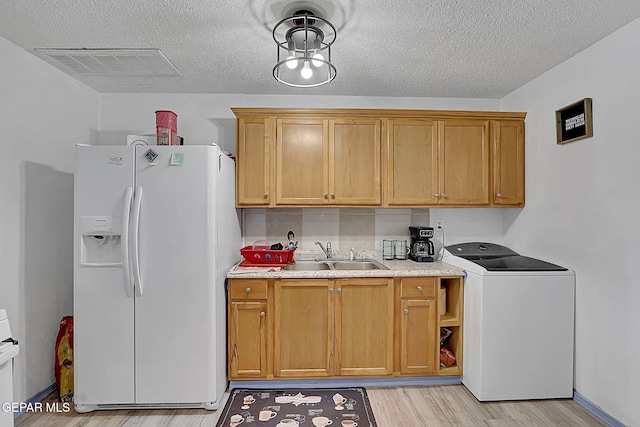 kitchen with light countertops, visible vents, white fridge with ice dispenser, a sink, and washer / dryer