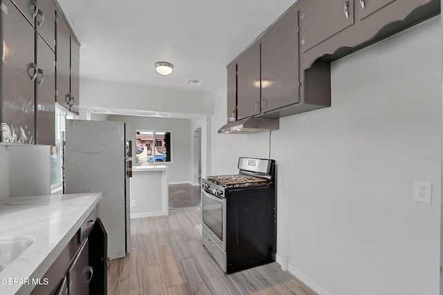 kitchen with under cabinet range hood, stainless steel gas stove, light wood finished floors, visible vents, and freestanding refrigerator