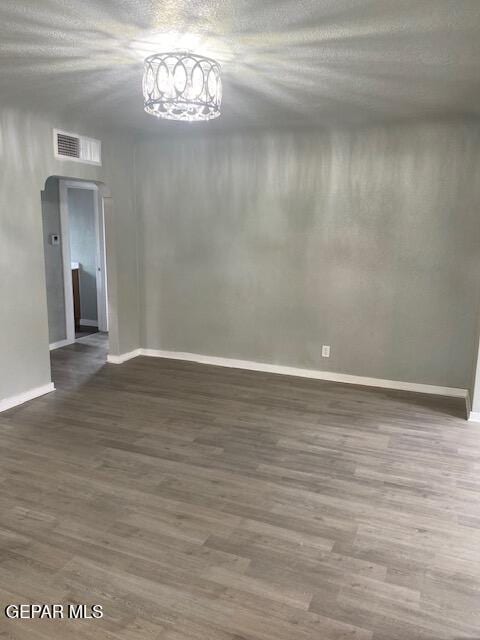 spare room with baseboards, visible vents, wood finished floors, and a chandelier