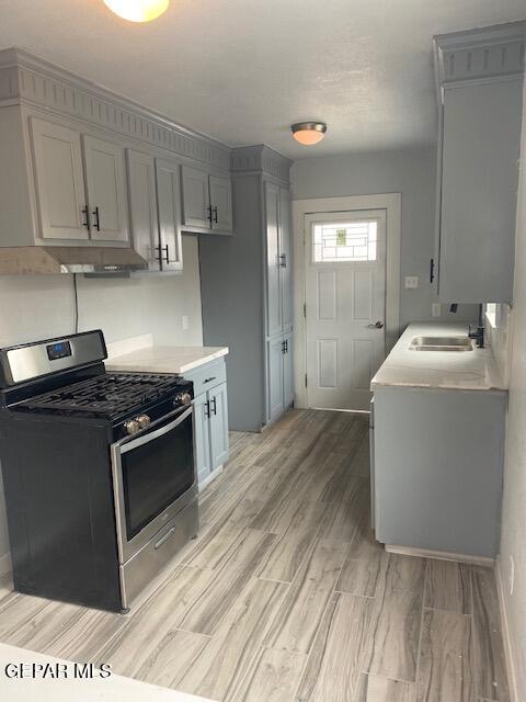 kitchen featuring light countertops, gray cabinets, a sink, stainless steel gas range, and light wood-style flooring