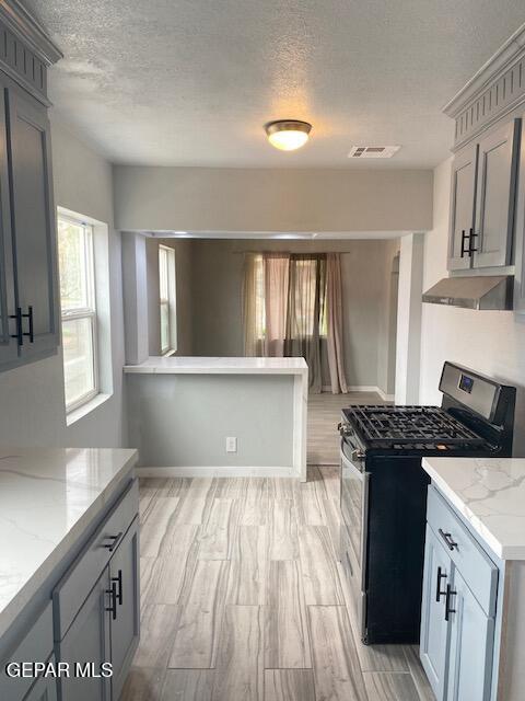 kitchen with light stone counters, ventilation hood, a textured ceiling, stainless steel gas range oven, and visible vents