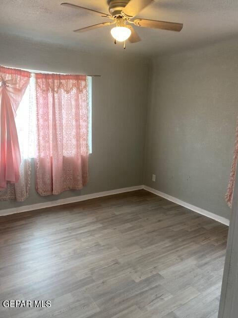spare room with a textured ceiling, baseboards, wood finished floors, and a ceiling fan