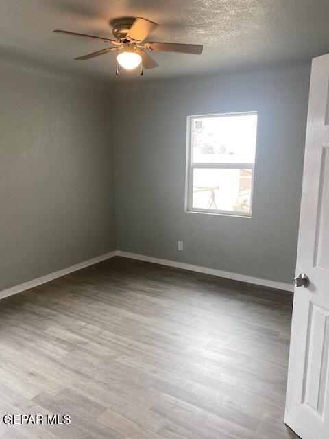 spare room featuring baseboards, wood finished floors, a textured ceiling, and a ceiling fan