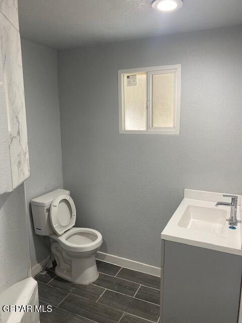 half bath with baseboards, toilet, and vanity