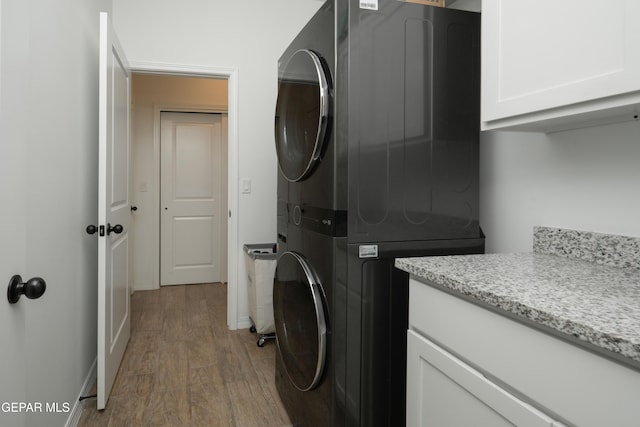 laundry area with stacked washing maching and dryer, baseboards, wood finished floors, and cabinet space