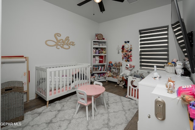 bedroom featuring a nursery area, visible vents, a ceiling fan, and wood finished floors