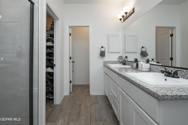 full bathroom featuring a spacious closet, double vanity, a sink, and wood finished floors
