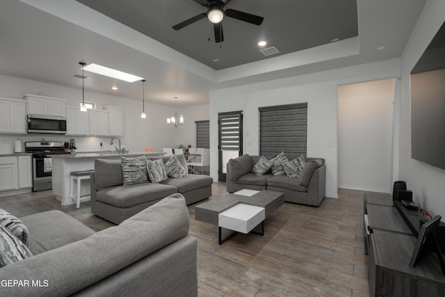 living room with recessed lighting, ceiling fan with notable chandelier, wood finished floors, and a raised ceiling