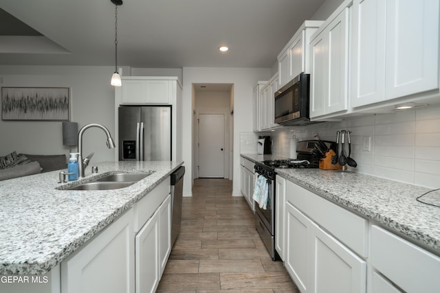 kitchen with hanging light fixtures, a sink, appliances with stainless steel finishes, white cabinetry, and backsplash