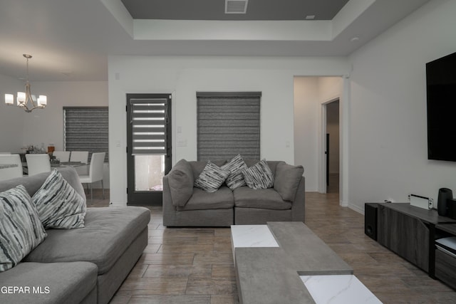 living room featuring a tray ceiling, wood finished floors, a notable chandelier, and visible vents