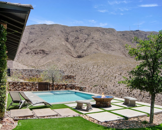 view of swimming pool featuring a fenced in pool, a fenced backyard, a mountain view, a patio, and a fire pit