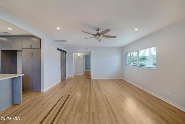 empty room with visible vents, light wood-style flooring, and a barn door