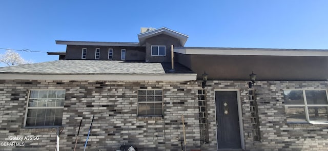 exterior space with roof with shingles and brick siding