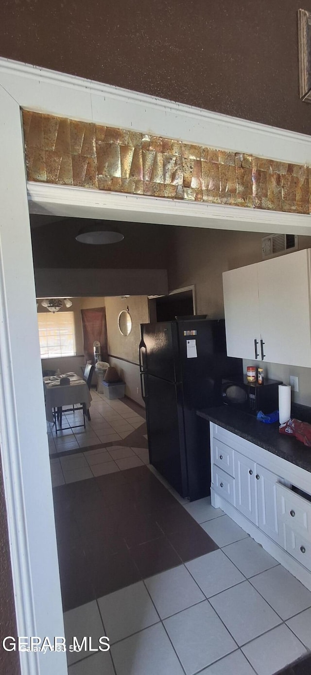 kitchen with dark countertops, light tile patterned floors, white cabinetry, and freestanding refrigerator