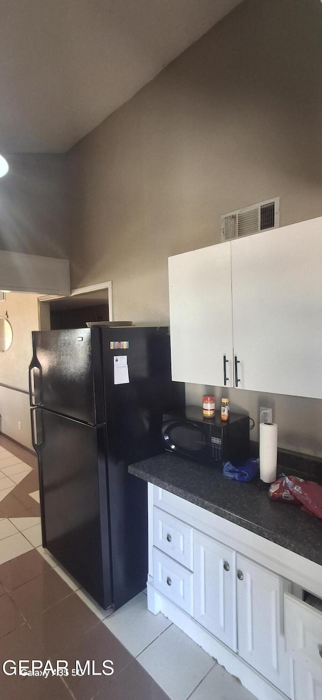 kitchen with light tile patterned floors, white cabinetry, black appliances, visible vents, and dark countertops